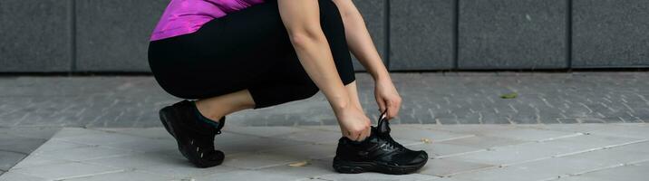 Fitness sport woman in fashion sportswear doing yoga fitness exercise in the city street over gray concrete background. Outdoor sports clothing and shoes, urban style. Sneakers closeup. photo