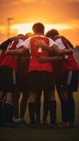 AI generated A group of young soccer players huddled together in a team talk, with the sun setting behind them photo