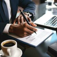 AI generated person hand holding a pen, signing a contract on desk with a laptop and coffee cup in the background photo