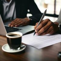 AI generated person hand holding a pen, signing a contract on desk with a laptop and coffee cup in the background photo