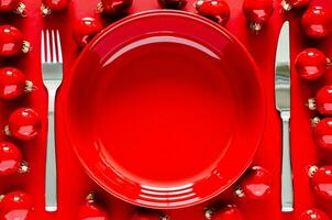 Red plate with knife and fork with red baubles on red background for Christmas holiday dining concept. photo