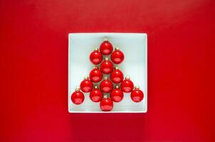 Red baubles set as Christmas tree shape put in white box on red background. Minimal Christmas holiday concept. photo