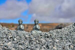 two small silver buddha statues sitting on a rocky cliff photo