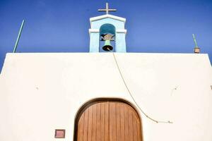 un blanco Iglesia con un campana torre y un de madera puerta foto