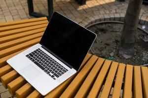 A laptop with empty screen stands on a wooden bench in the courtyard, workspace of freelancer in beautiful home garden photo