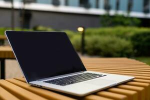 A laptop with empty screen stands on a wooden bench in the courtyard, workspace of freelancer in beautiful home garden photo