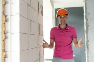 profession, construction and building - happy smiling worker or builder in helmet over room with working equipment at new home or apartment background photo