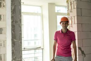 profesión, construcción y edificio - contento sonriente trabajador o constructor en casco terminado habitación con trabajando equipo a nuevo hogar o Departamento antecedentes foto