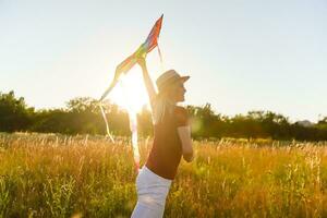 Happy young woman running with a kite on a glade at sunset in summer photo