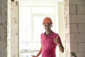 profesión, construcción y edificio - contento sonriente trabajador o constructor en casco terminado habitación con trabajando equipo a nuevo hogar o Departamento antecedentes foto