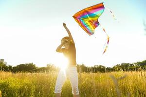 Happy young woman running with a kite on a glade at sunset in summer photo