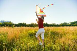 Portrait of a young and carefree woman launching kite on the greenfield. Concept of active lifestyle in nature photo