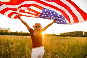 hermosa joven niña participación un americano bandera en el viento en un campo de centeno. verano paisaje en contra el azul cielo. horizontal orientación. foto