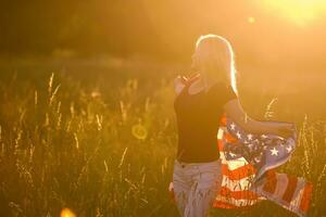 Beautiful young girl holding an American flag in the wind in a field of rye. Summer landscape against the blue sky. Horizontal orientation. photo