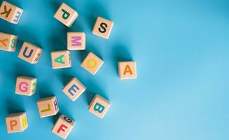 vistoso de madera cubitos con letras dispersado en azul antecedentes. aprendiendo, creciente iq, desarrollo para niños. parte superior ver de para niños juguetes educativo juegos. foto