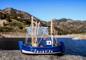 a toy boat sitting on a rock near a lake photo