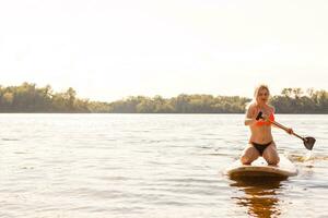 joven atractivo mujer en estar arriba paleta tablero en el lago, cenar foto