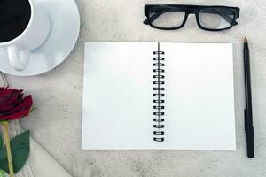 Note book with pen, reading glasses, coffee and roses on marble table. photo