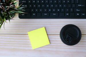 Sticky note with disposable coffee cup, computer keyboard and potted plant. photo