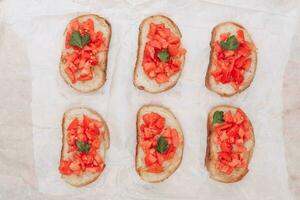 Delicious bruschetta, toasted bread with tomatoes on white paper, top view photo