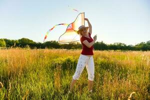 retrato de un joven y despreocupado mujer lanzamiento cometa en el campo verde. concepto de activo estilo de vida en naturaleza foto