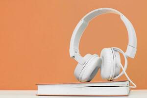 audio libro concepto con auriculares y un libro en un melocotón pelusa antecedentes. escuchando a un libro. foto