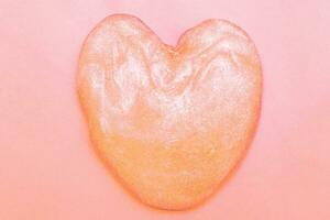 Peach Fuzz glitter slime in the form of a heart on pink background. photo