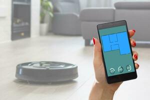 Close-up Of A woman Holding Remote Control Of Robotic Vacuum Cleaner To Start Cleaning photo