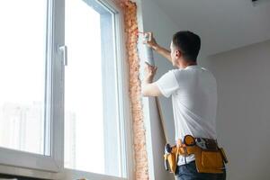 hombre poniendo relleno Entre ventana y pared en un nuevo casa foto