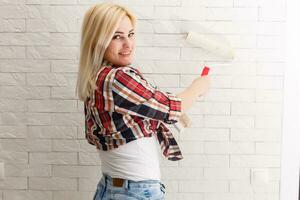 Woman painting wall in new home. Happy beautiful young woman doing wall painting. A young girl makes repairs paints the walls with white paint using a roller. photo