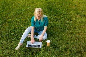 Top view of woman sitting in park on the green grass with laptop, hands on keyboard. Computer screen mockup. Student studying outdoors. Copy space for text photo