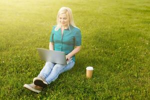 Top view of woman sitting in park on the green grass with laptop, hands on keyboard. Computer screen mockup. Student studying outdoors. Copy space for text photo