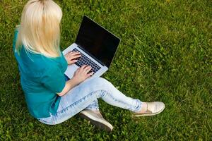 beautiful young blond woman with a laptop in the park on a warm summer day photo