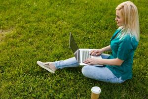 Top view of woman sitting in park on the green grass with laptop, hands on keyboard. Computer screen mockup. Student studying outdoors. Copy space for text photo