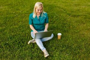 Top view of woman sitting in park on the green grass with laptop, hands on keyboard. Computer screen mockup. Student studying outdoors. Copy space for text photo