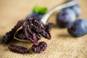 Dried prunes in a spoon on a burlap tablecloth against a background of fresh plums. photo