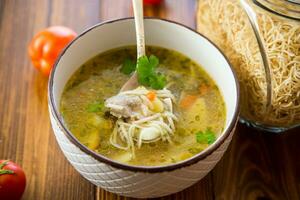 Chicken noodle soup with parsley and vegetables in a white plate photo