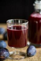 plum red wine in a glass and a decanter against the background of ripe large plums photo