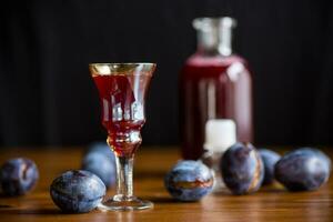 plum red wine in a glass and a decanter against the background of ripe large plums photo