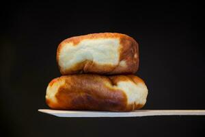 Fried pies filled with yeast dough on a wooden paddle, isolated on a black background. photo