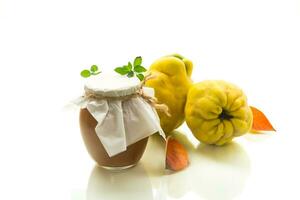 Ripe quince fruit with jam in a glass jar isolated on a white background. photo