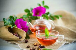 elaborada rosa mosqueta té en un vaso tetera con rosa mosqueta flores y menta foto