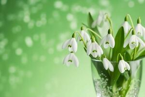AI generated a bouquet of snowdrops in a transparent tequila glass. splashes of water on petals. first spring flowers. forest. hello spring. women's day concept. green blur background. generative ai. photo