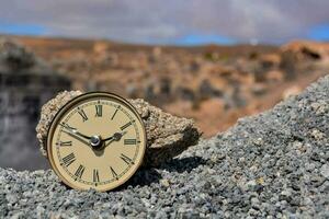 a small clock sits on top of a rock in the desert photo