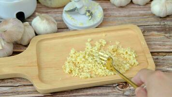 A man's hand uses a spoon to arrange crushed garlic into a wooden plate. video