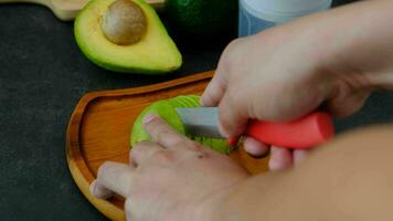männlich Hände Schneiden Avocado Fleisch in schön Vereinbarungen auf ein hölzern Platte. video