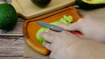 männlich Hände Schneiden Avocado Fleisch in schön Vereinbarungen auf ein hölzern Platte. video