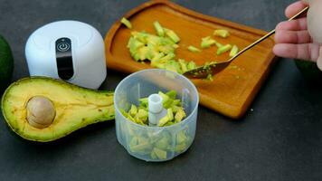 A man's hand is putting avocado pulp into a blender bowl. video