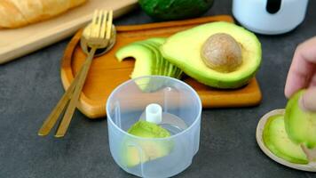 A man's hand is putting avocado pulp into a blender bowl. video