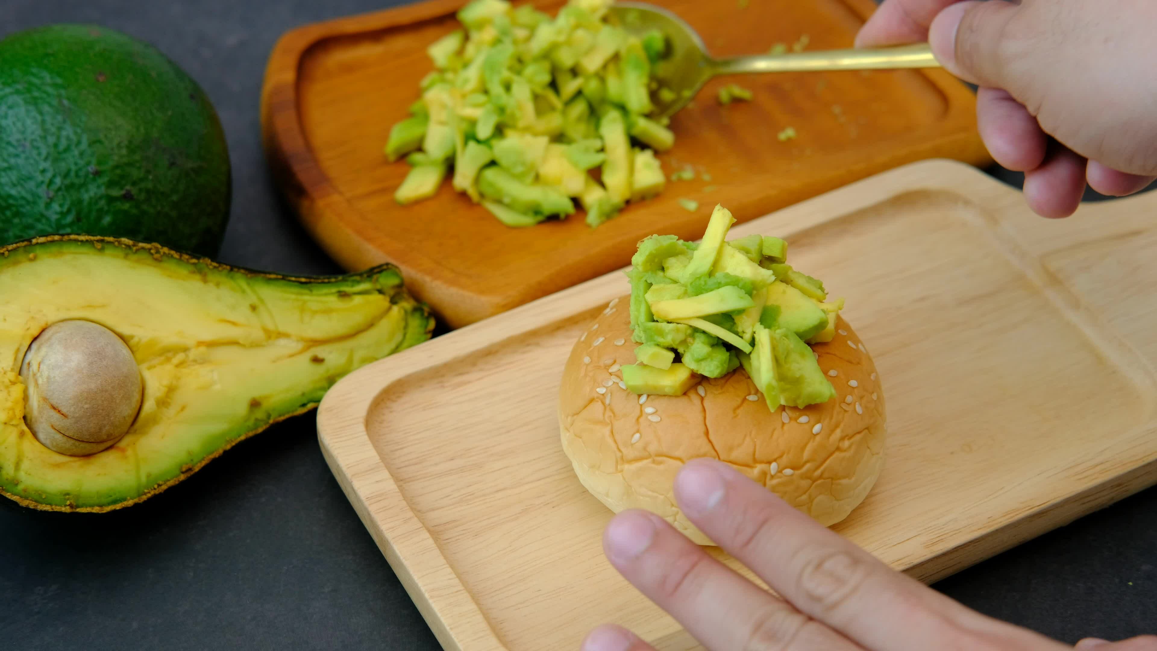 A man's hand scoops out mashed avocado pulp and places it on a loaf of